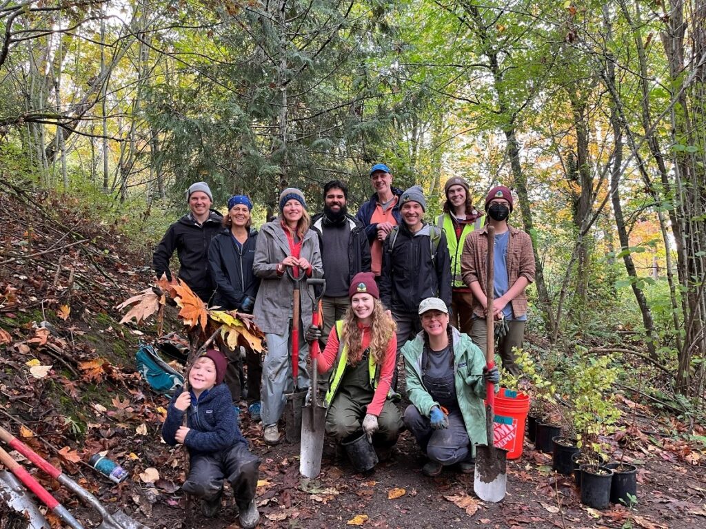 11 people posing for a photo with shovels and potted trees.