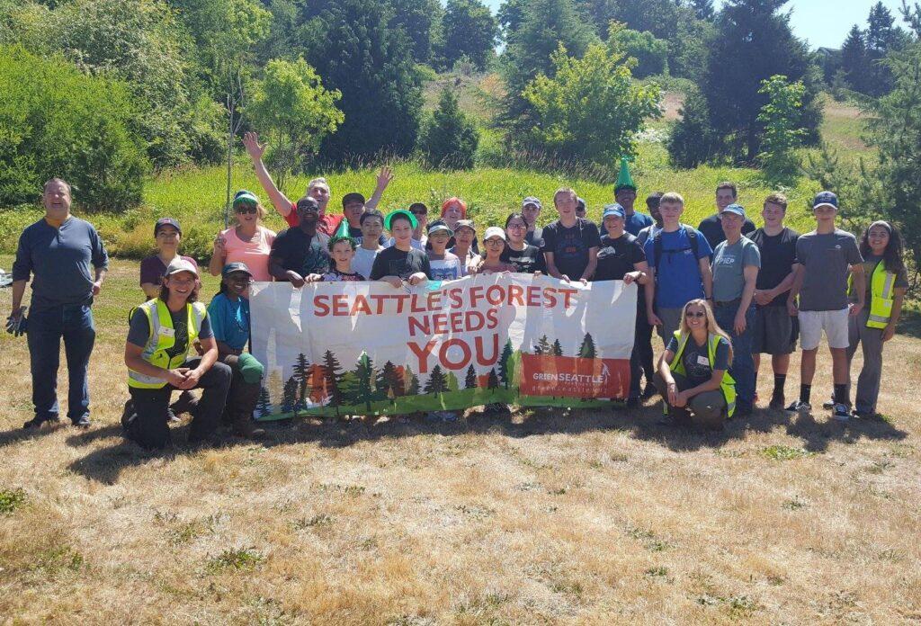 A large group of people posing for a photo holding a banner that reads, ' Seattle's Forest Needs You'