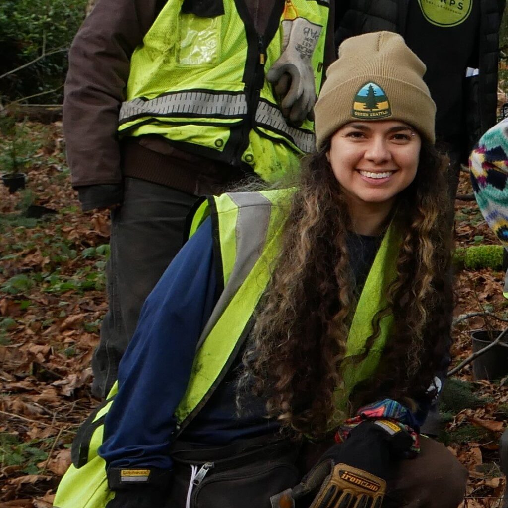 Gabi kneeling in a forest, wearing a high visibility vest.