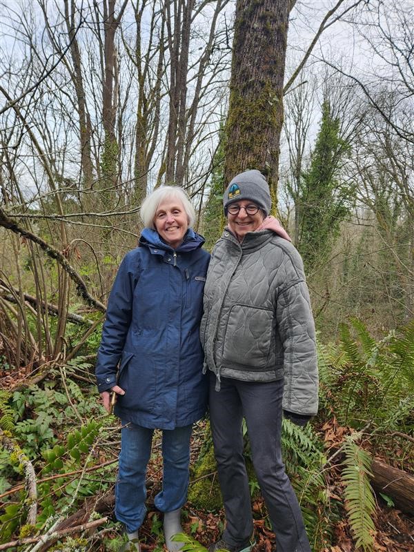 Beth and Jeanne standing among ferns and mossy trees.